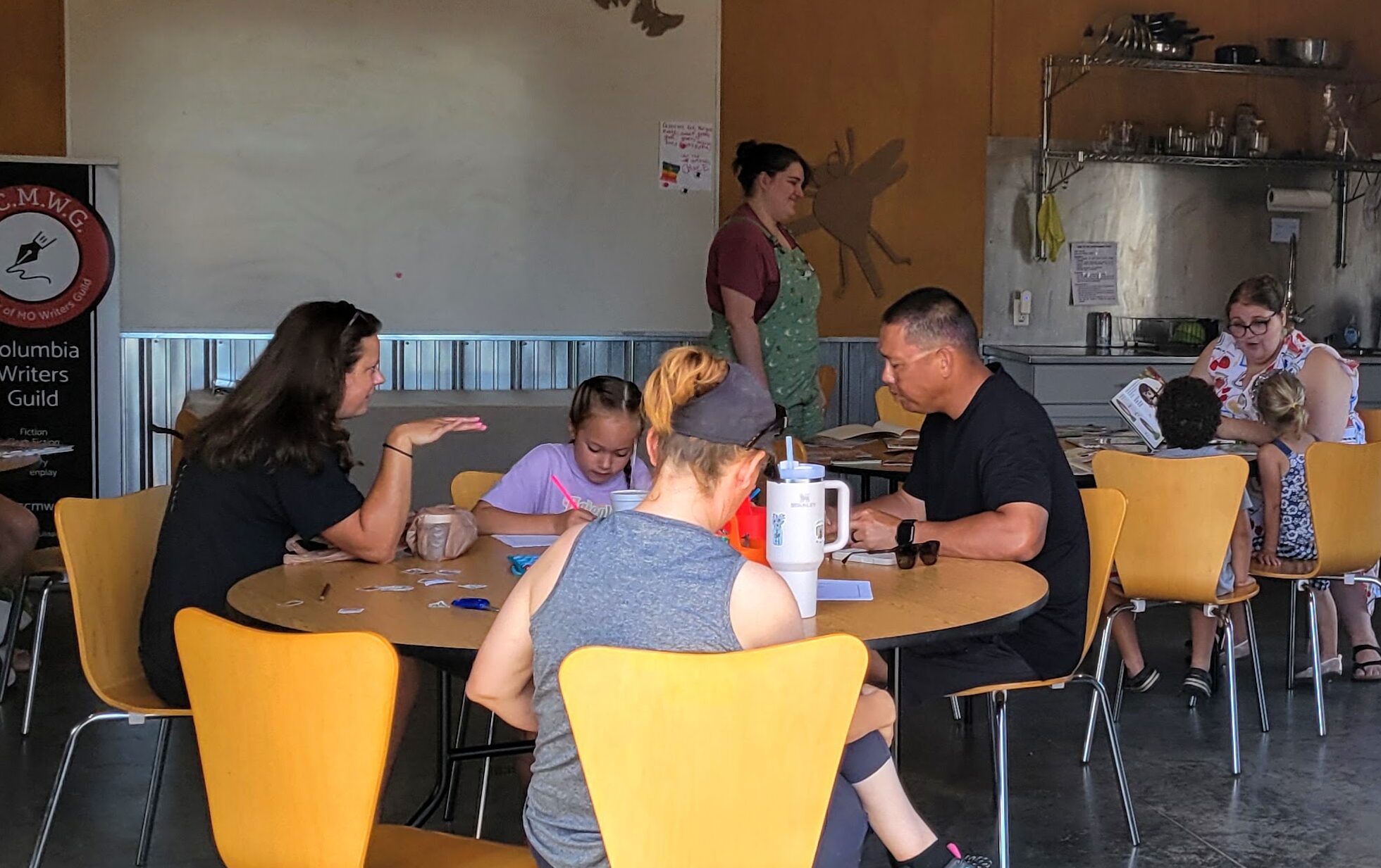 People around tables participating in the event. Farmer's Market CCMWG Booth, July 2026.